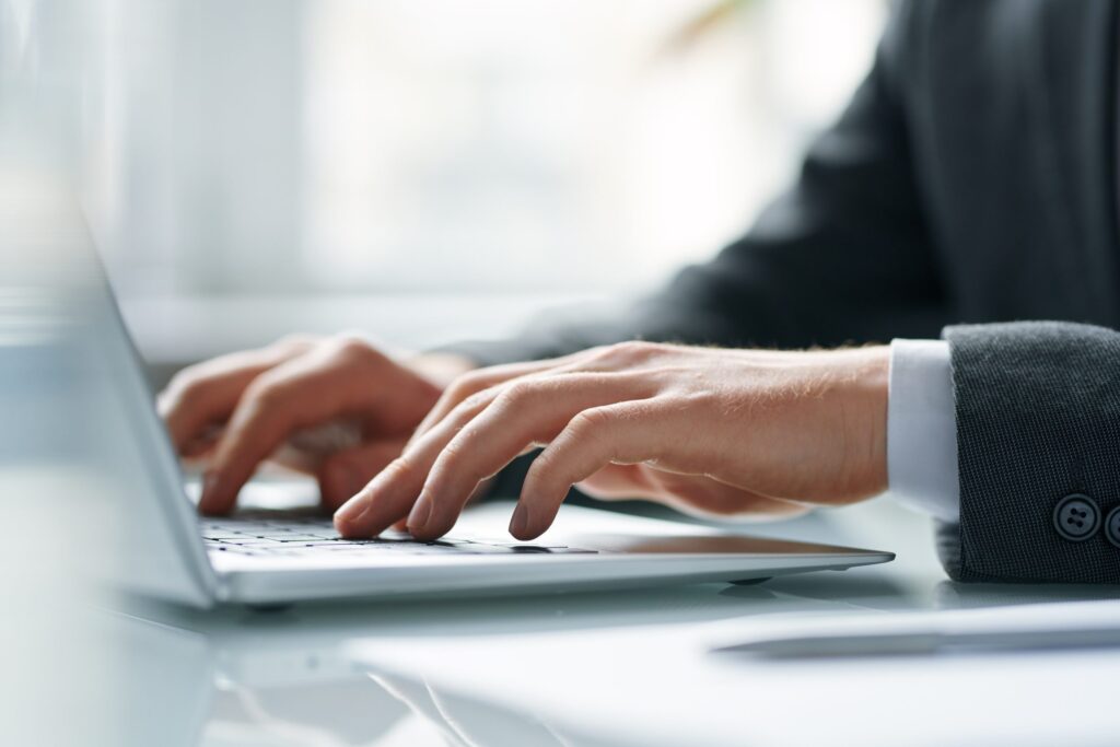 Hands of contemporary mobile broker pushing keys of laptop keypad